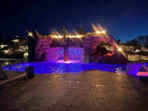 swimming pool grotto with landscape lighting, water fall, and slide features