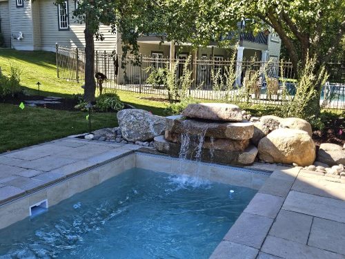 Plunge pool with stone waterfall feature and paver patio in landscaped backyard